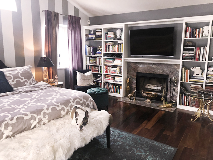 grey and white bedroom with striped accent wall and fireplace and built-in bookshelves