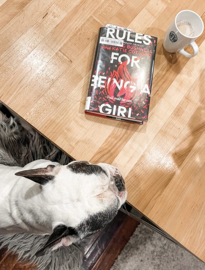 french bulldog sits at counter with book rules for being a girl by candace bushnell and katie cotugno with coffee in the kitchen