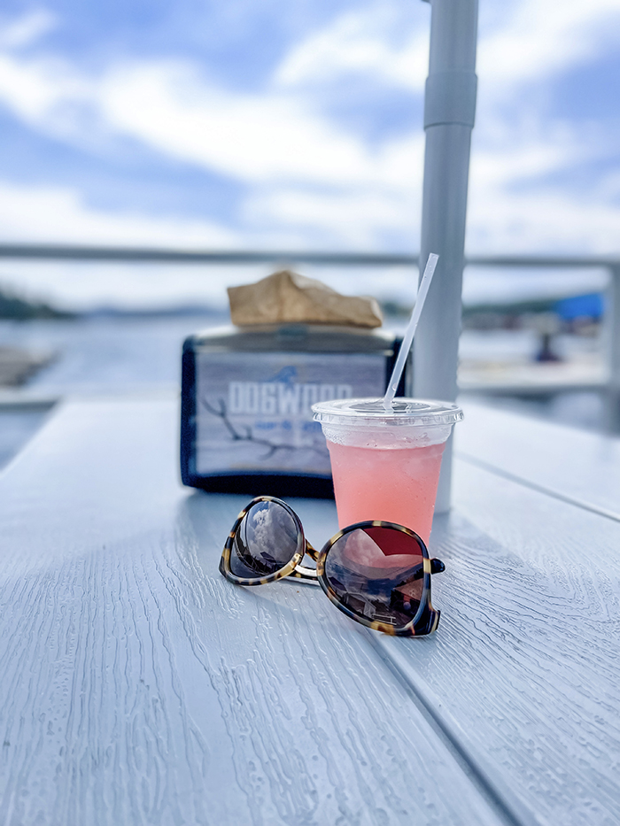 pink lemonade, tortoise shell sunglasses sitting on a table in front of the blue water and sky, dogwood dockside bar and grill at the lake arrowhead marina