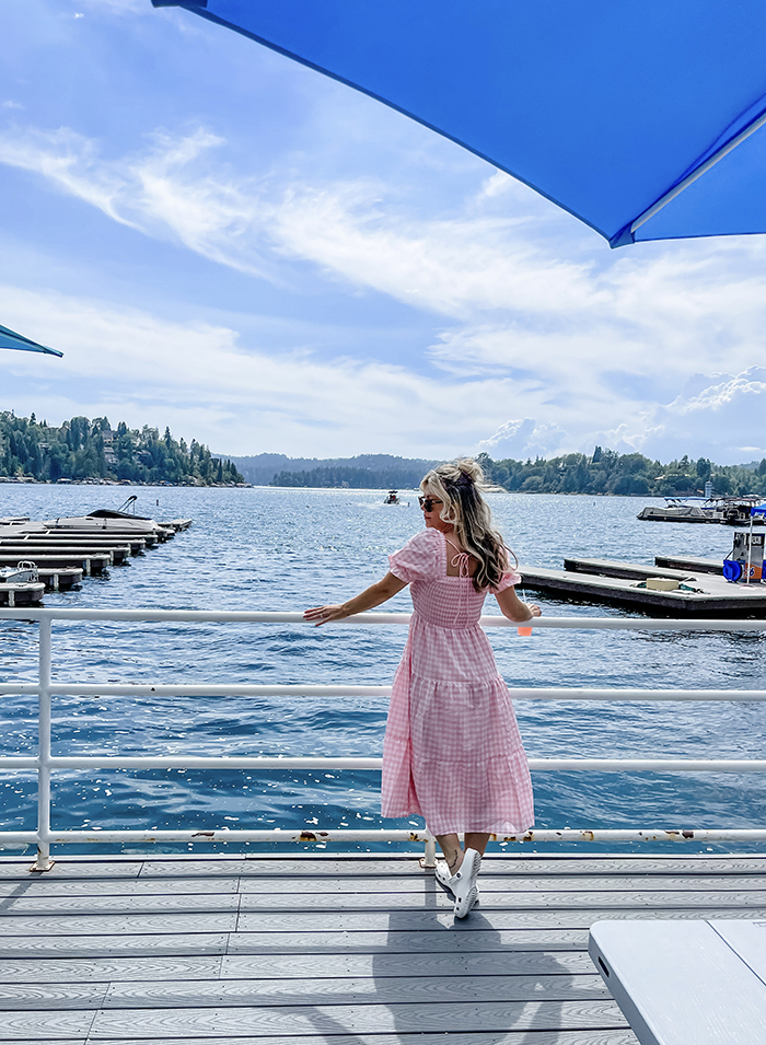 pink and white checkered maxi dress with smocked bodice and big puffy sleeves, maegan tintari, owner of dogwood dockside standing on the dock at the lake arrowhead marina in a pink dress and white crocs