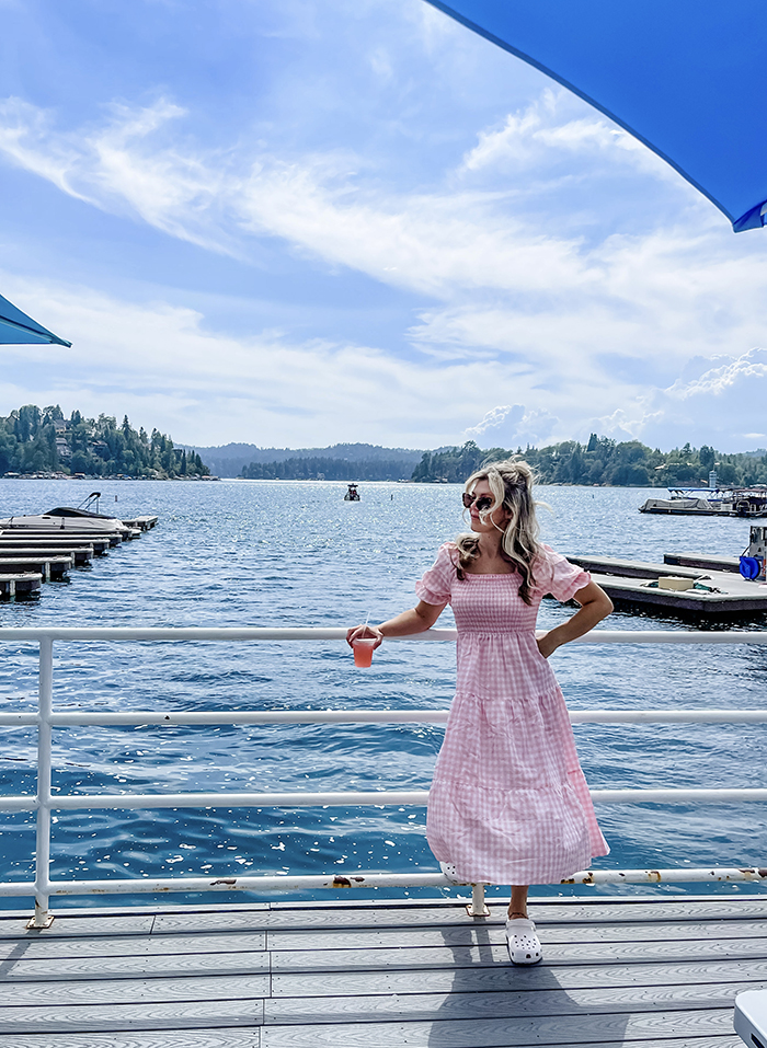 pink and white checkered maxi dress with smocked bodice and big puffy sleeves, maegan tintari, owner of dogwood dockside standing on the dock at the lake arrowhead marina in a pink dress and white crocs