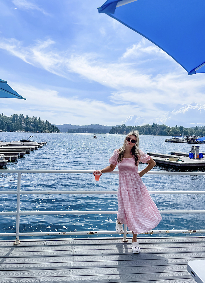 pink and white checkered maxi dress with smocked bodice and big puffy sleeves, maegan tintari, owner of dogwood dockside standing on the dock at the lake arrowhead marina in a pink dress and white crocs