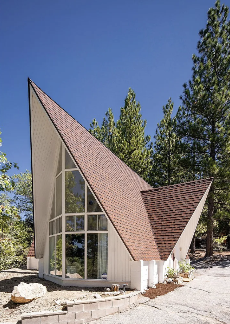 cute little apple a-frame white cabin in the woods with pink door