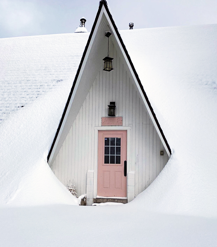 little-apple-a-frame-white-cabin-pink-door-in-the-mountains-lake-arrowhead-running-springs-in-the-snow-winter