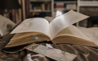 open book on bed with book light