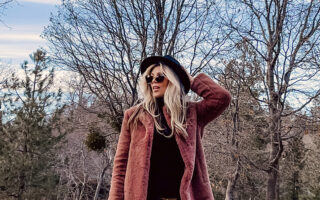 casual 70s boho look-floral bell bottom flares-faux fur coat-blonde woman standing on a tree-lined street with fall colors and leaves and blue cloudy skies