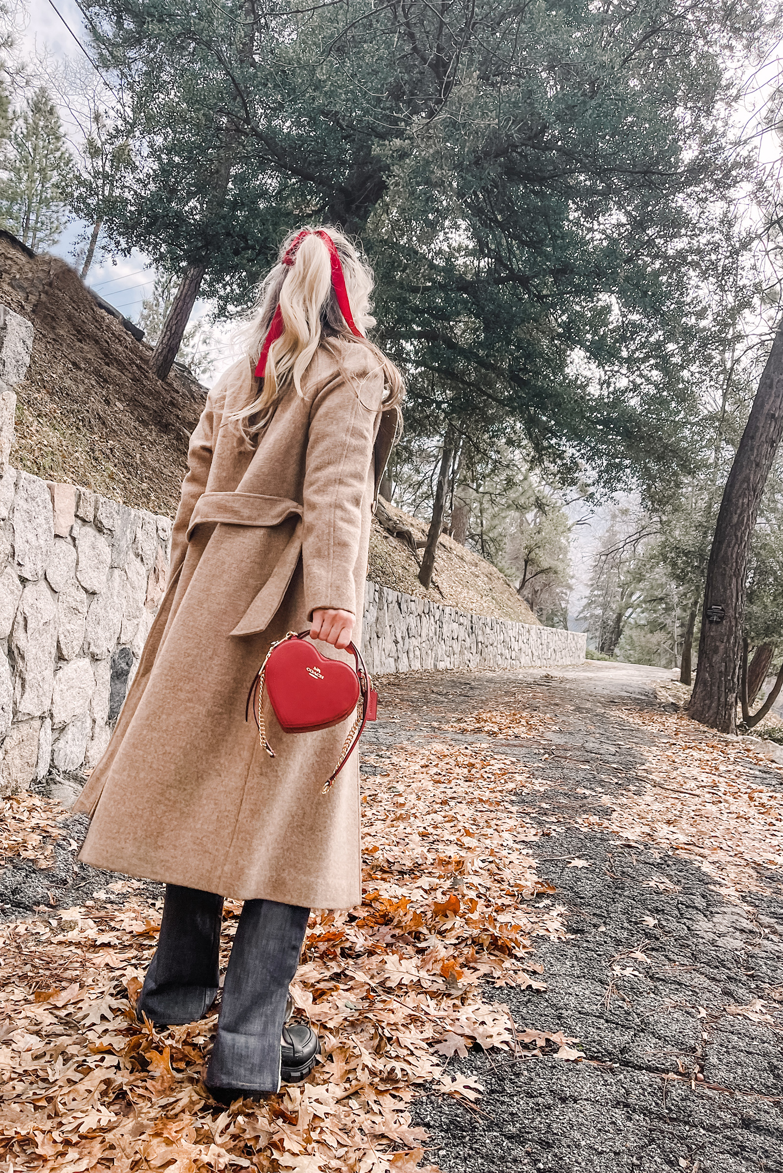 red heart shaped coach bag for valentine's day, casual outfit, vintage levis jeans with a hem slit, chunky loafers, leopard print sweater, red ribbon in her hair, blonde waves, casual winter style