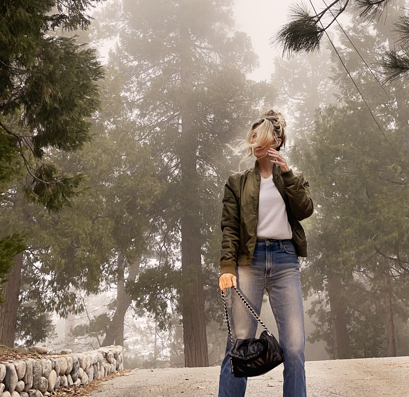 casual denim style, straight classic high waist ankle jeans, army green jacket and nike shoes with vintage white sweater and black pillow bag, spring 2024 style in the forest fog