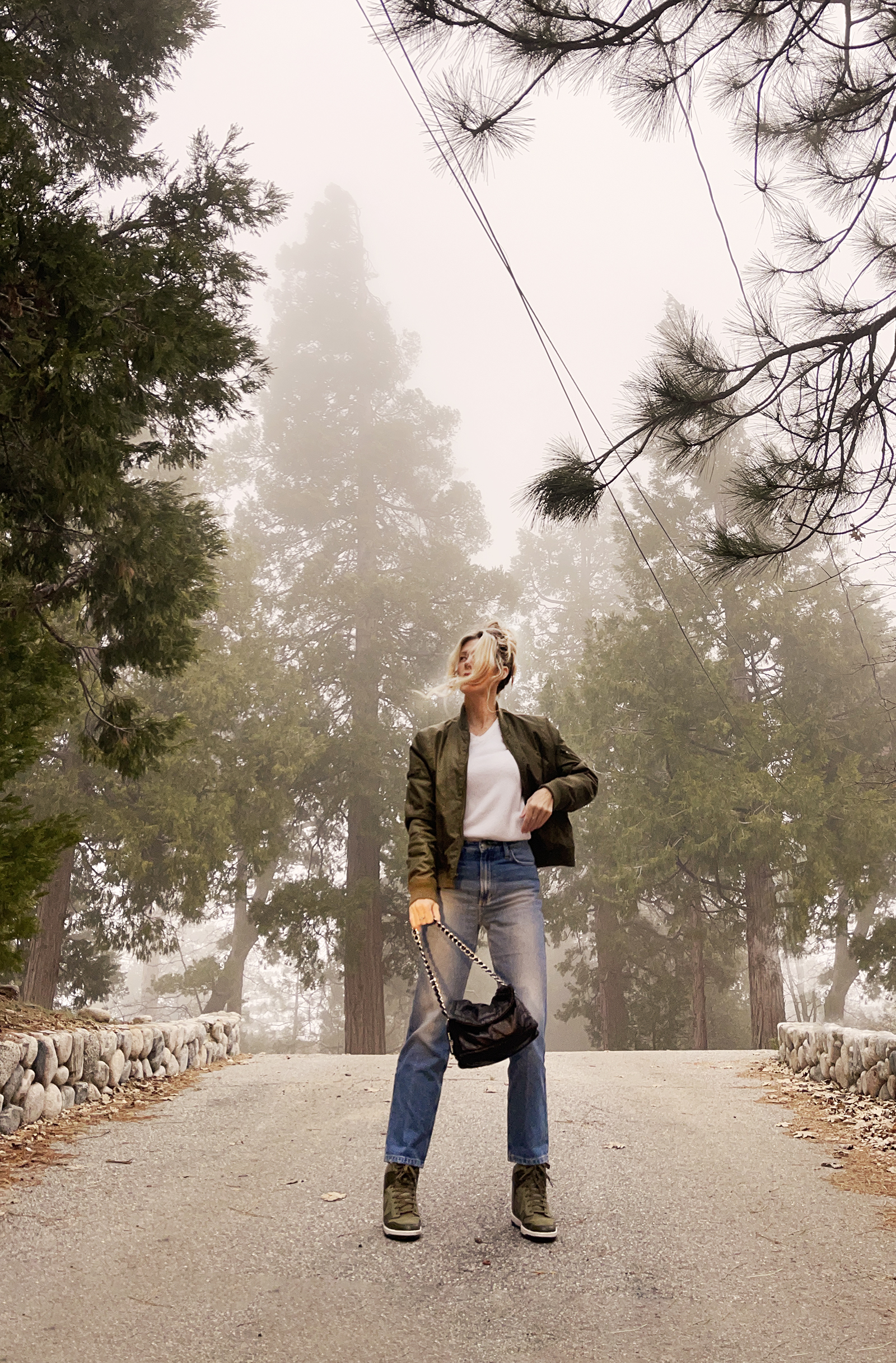 casual denim style, straight classic high waist ankle jeans, army green jacket and nike shoes with vintage white sweater and black pillow bag, spring 2024 style in the forest fog